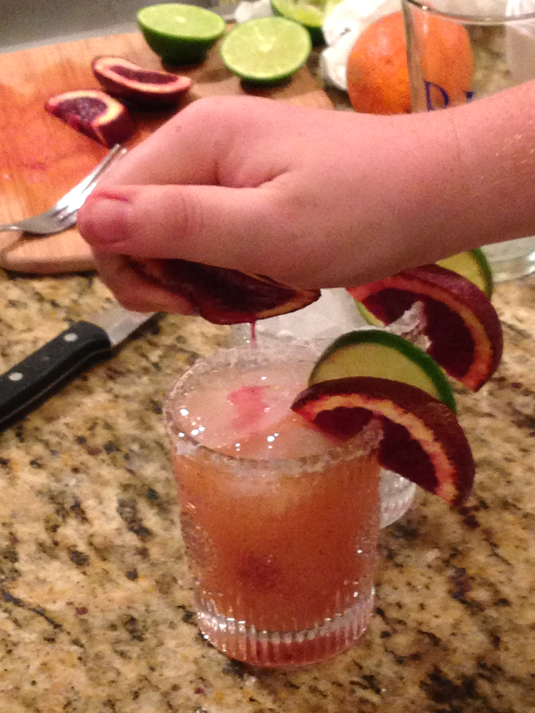 Squeezing blood orange over margaritas
